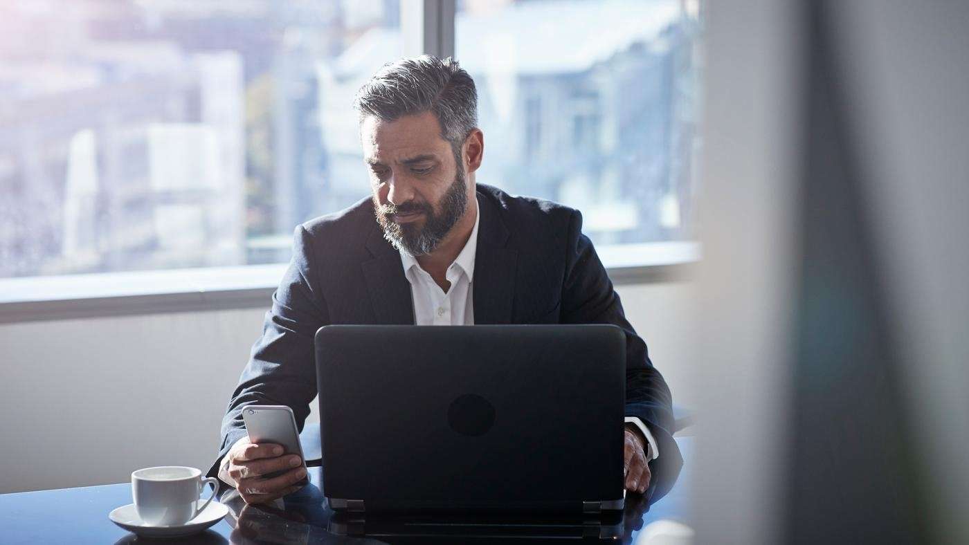 Modern chic business people working in an incredible modern & original office space. A man uses his smartphone and laptop.