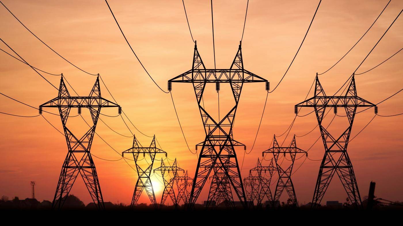 Three rows of electricity pylons against a deep orange sunset sky.