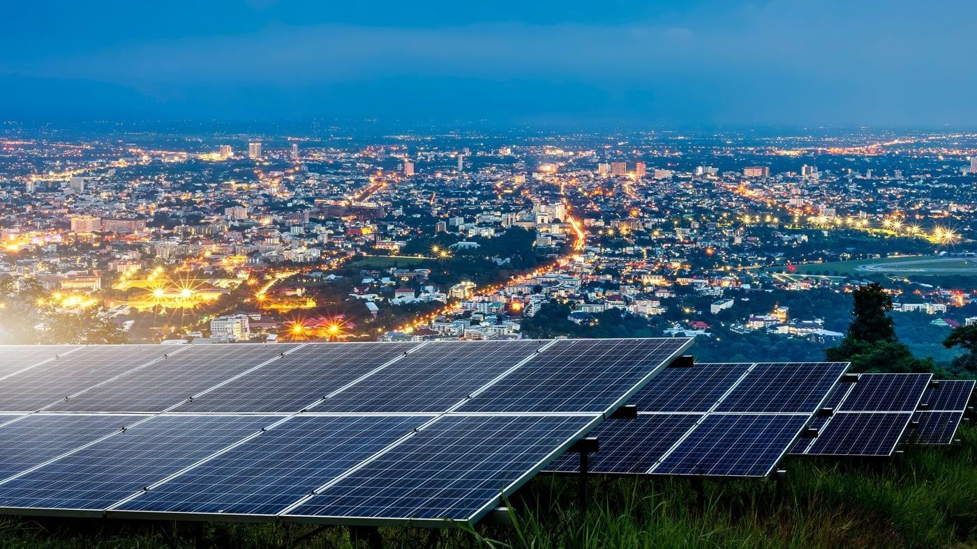 Solar panels on top of a hill overlooking an illuminated city at night.