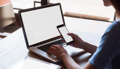 Multitasking woman using tablet, laptop and smart phone, with blank screens, indoors on a table.