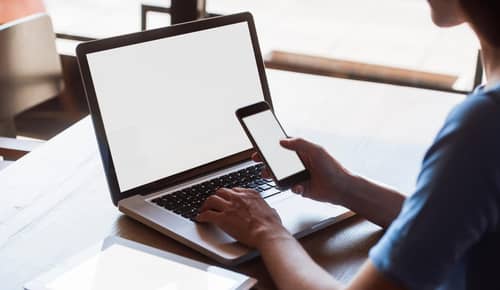 Multitasking woman using tablet, laptop and smart phone, with blank screens, indoors on a table.
