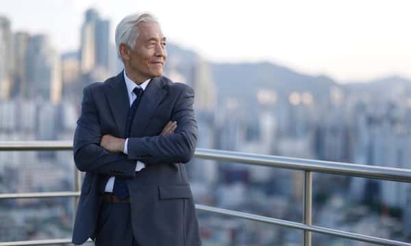 A man in a suit is standing on a balcony overlooking a city.