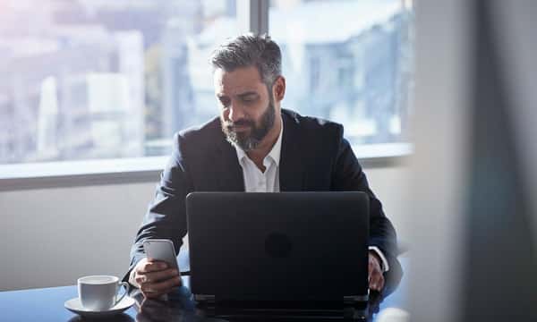 Modern chic business people working in an incredible modern & original office space. A man uses his smartphone and laptop.