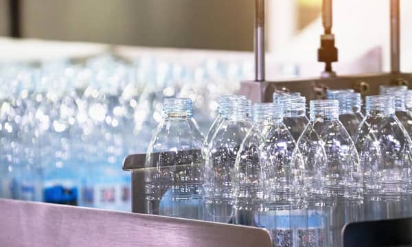 Several batches of empty white plastic bottles, being processed on a conveyor belt.