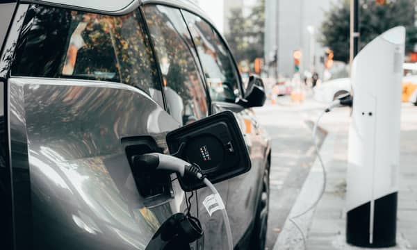 Car parked a busy urban street, plugged into an electric vehicle charging station.