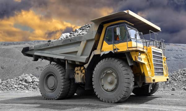 A yellow dump truck filled with rocks, is parked in front of a dark cloudy sky.