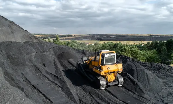 A yellow digger is mining rocks in next to rolling countryside hills.