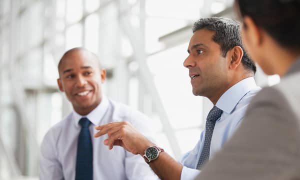 Three business people, smartly dressed, talking in an office.