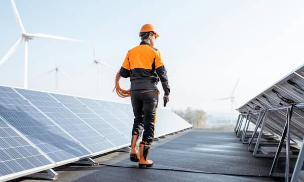 A worker standing on a roof next solar panels and wind turbines.