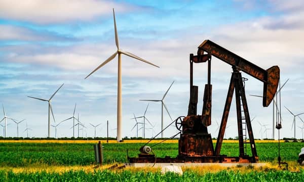 An oil well and wind turbines in a field.