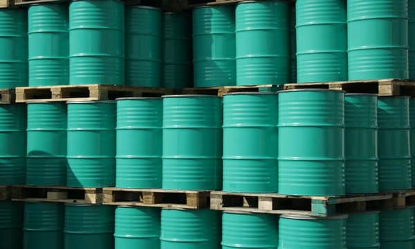 Pile of green industrial barrels stored outside a warehouse.