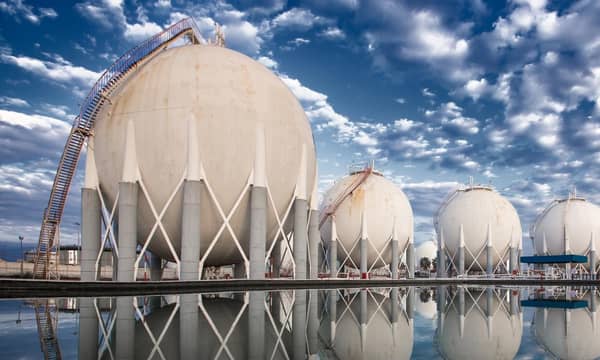 Four LNG storage tanks, reflecting in the body of water they stand at.
