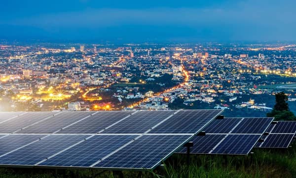 Solar panels on top of a hill overlooking an illuminated city at night.