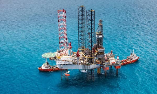 An aerial view of an oil rig and two tankers in the ocean.