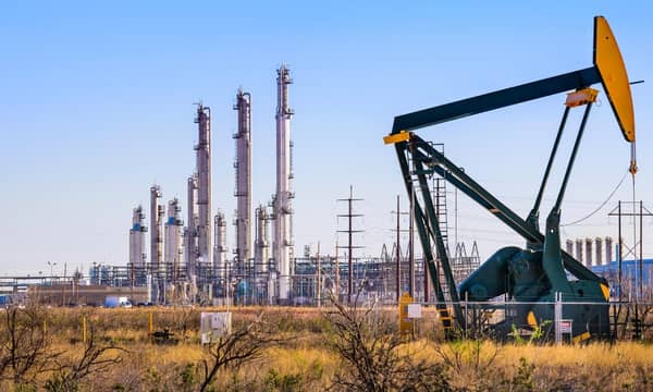 An oil pump in front of an oil refinery, with a network of electricity pylons.