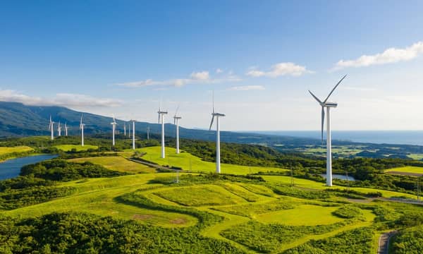 A row of wind turbines in the mountain coastal cliffs, under the blue sky.