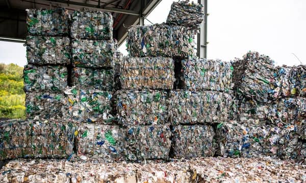 Multiple stacked bales of plastic waste, in an open-sided warehouse.