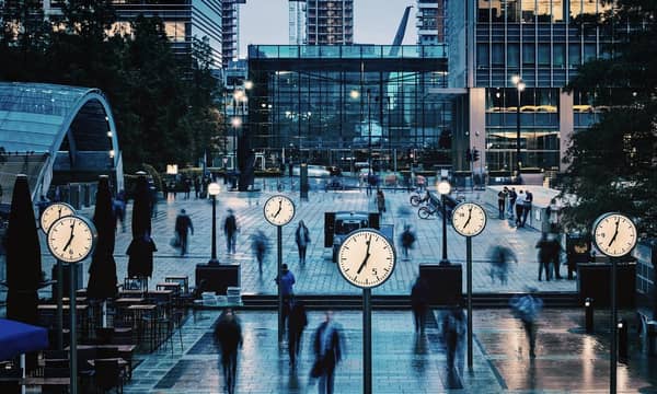 Blurred People walking and clocks in front of Canada Square, Canary Wharf, London.