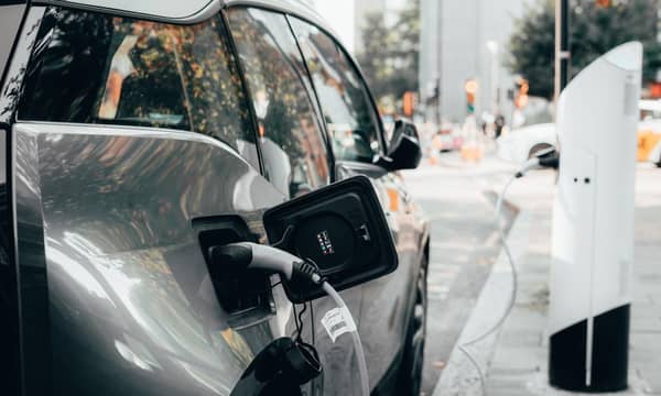 Car parked a busy urban street, plugged into an electric vehicle charging station.