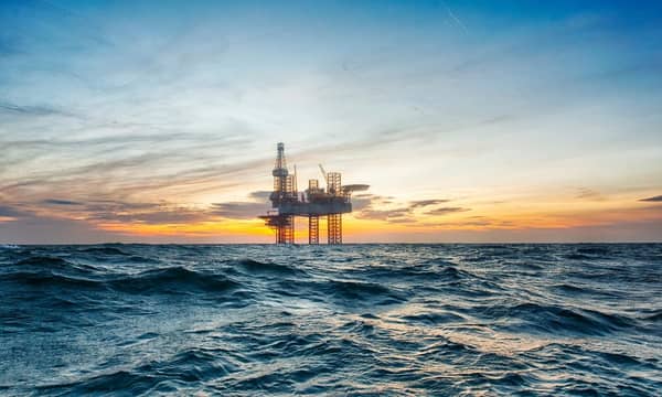 A close-up of an oil rig in the middle of open choppy waters, during an orange sunset.