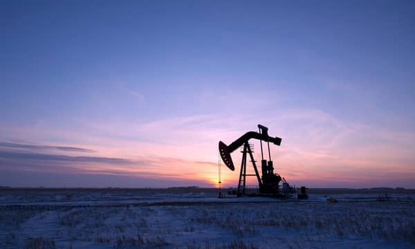 An oil pump in a vast snow covered field at sunset.