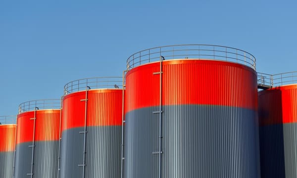 Multiple rows of connected red and grey storage tanks, with a blue sky with copy space in the background.