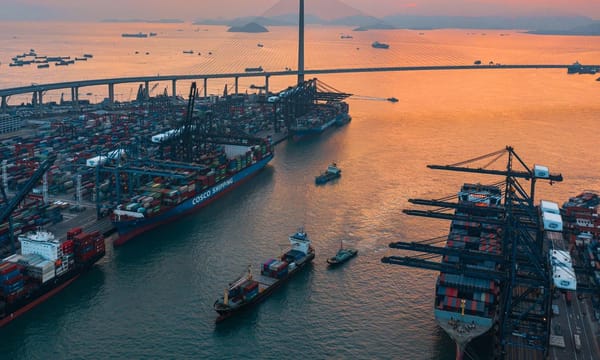 A vast container port with large ships of cargo, next to a long modern suspension bridge.