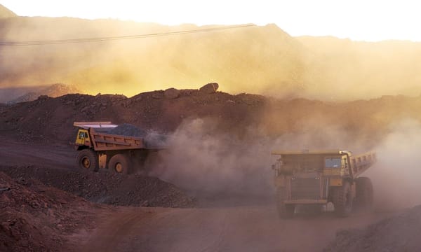Two dump trucks driving down a dirt road in a quarry.