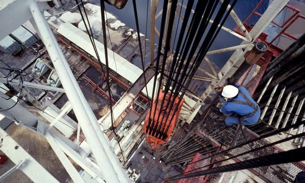 An aerial view of a central column of a drilling rig, with a worker checking the hoist.