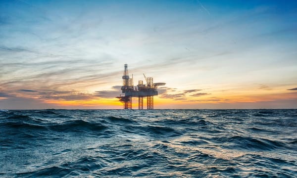 A close-up of an oil rig in the middle of open choppy waters, during an orange sunset.