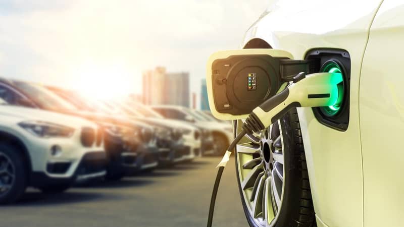 A yellow electric vehicle charging in a car park, a row of BMW cars to one side.