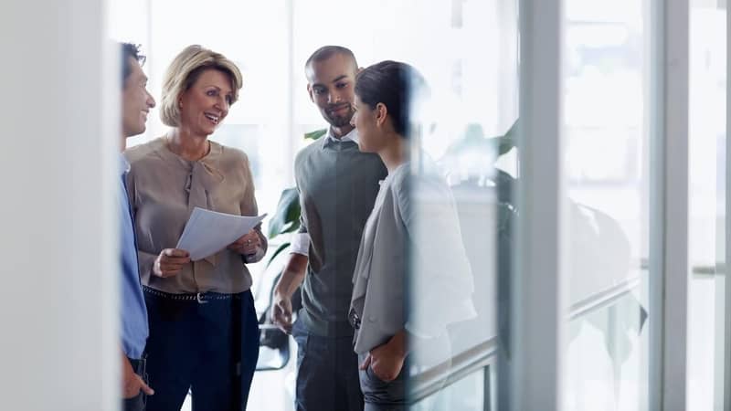 Smiling businesswoman discussing over document with colleagues in office.
