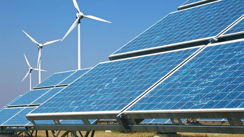 Solar panels and wind turbines in a field, against a clear blue sky.