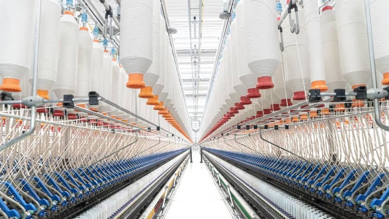 The interior of a factory with hundreds of raised spindles, weaving fibres from the machinery below.