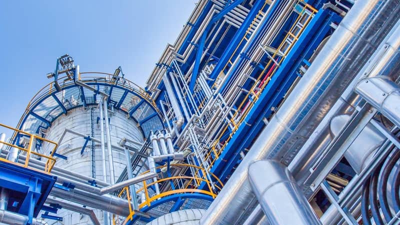 The exterior of an industrial plant with blue and yellow platforms, around a large metal cylindrical tank.
