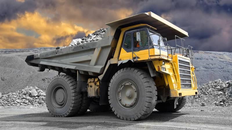A yellow dump truck filled with rocks, is parked in front of a dark cloudy sky.