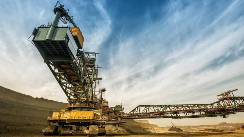 A large crane is in the middle of a quarry/mine, against a blue sky.