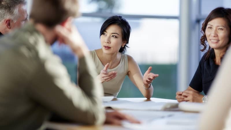 A group of people sitting around a table in a meeting, one lady is engrossed by the conversation.
