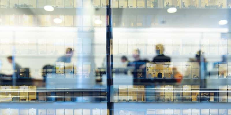 Workers working late. Tall building reflected by lights on the glass facade.