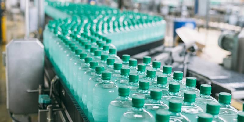 A line of green bottles on a conveyor belt in a factory.
