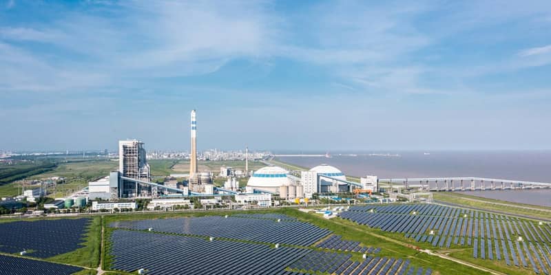 An aerial view of a solar power plant on a coastline, next to the sea and blue skies.