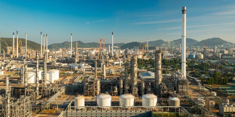 An aerial view of an oil refinery with mountains and clear blue skies in the background.