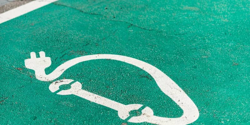 Close-up of electric vehicle charge bays green coloured asphalt, with white painted charging symbol.