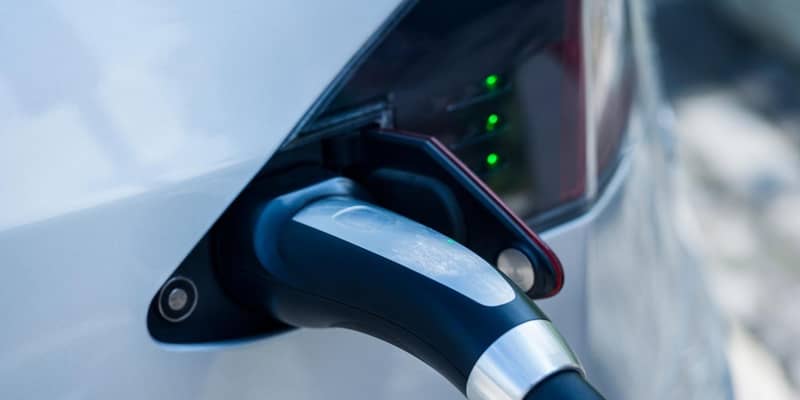 Close-up if an electrical vehicle charging cable, plugged into the side of a car.