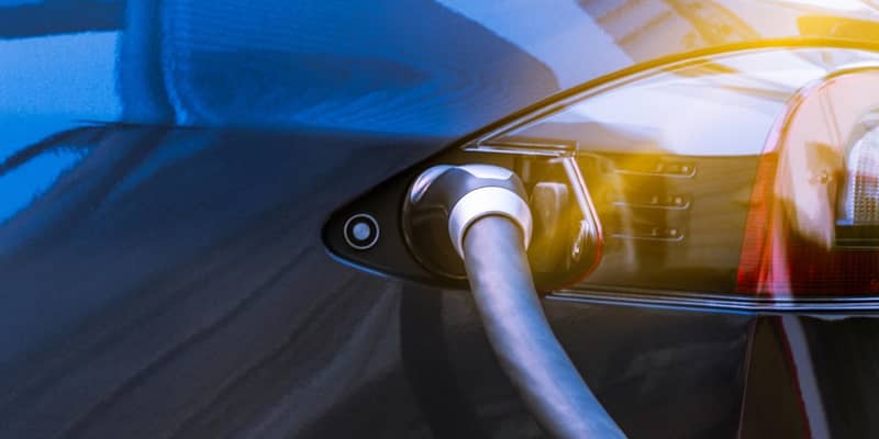 Electric vehicle charging cable plugged into the side of a black car.