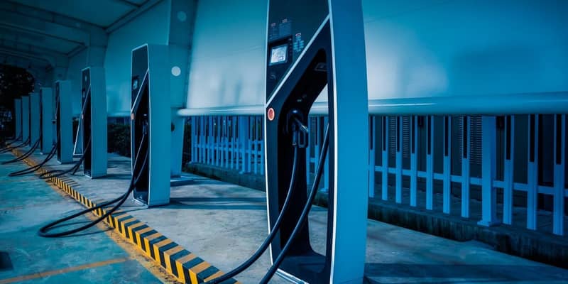 A row of modern electric vehicle charging stations, in a covered parking bay at night.