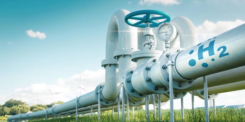 3D render of hydrogen pipelines in a field with wind turbines in the distance.