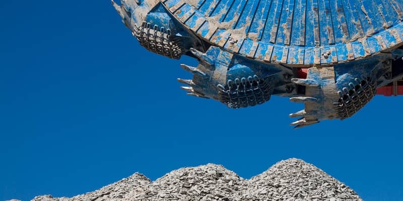 A blue excavator in the working a pile of rocks.