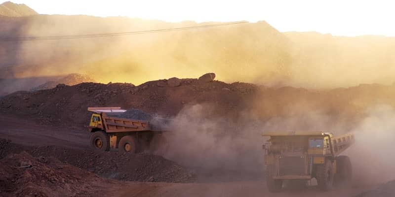 Two dump trucks driving down a dirt road in a quarry.