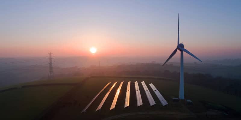 An aerial view of solar panels and a wind turbine in a field at sunset.